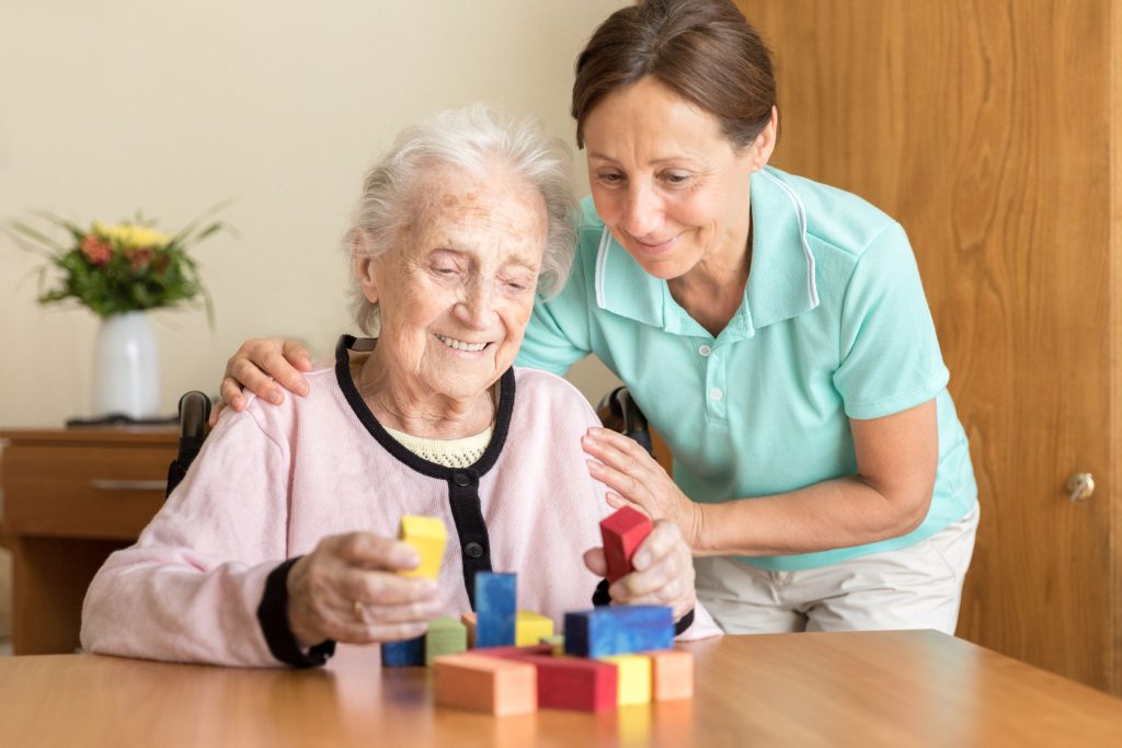 קשישה מרכיבה מגדל מקוביות ולידה המטפלת