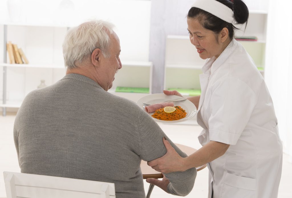 מטפלת זרה מגישה אוכל לקשיש