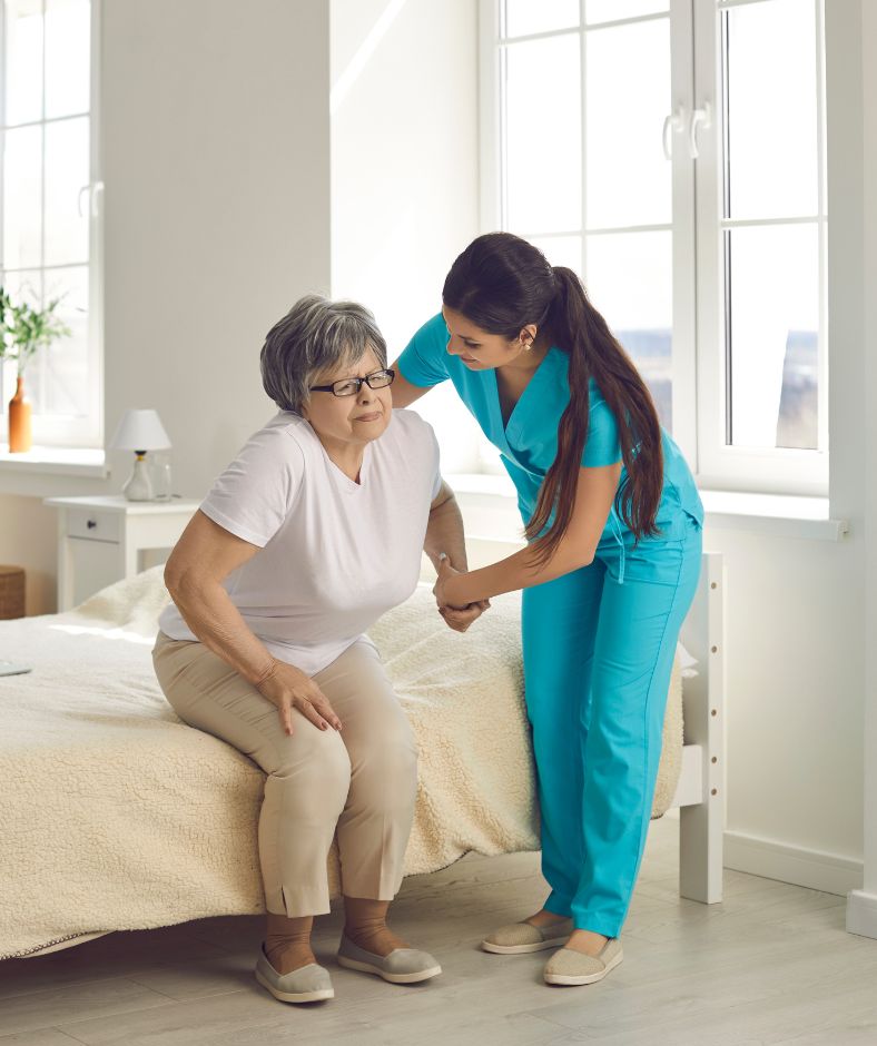 מטפלת עוזרת לקשישה לקום מהמיטה