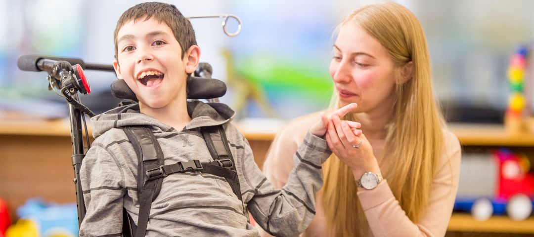 ילד נכה בכיסא גלגלים ולידו סייעת