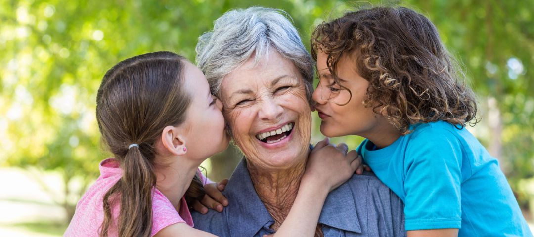 קשישה עם שני נכדים לצידה - נותנים לה נשיקה על הלחי מכל צד