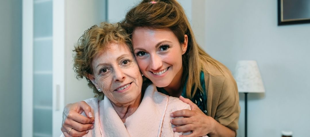 קשישה ואישה צעירה בחיבוק אל מול המצלמה