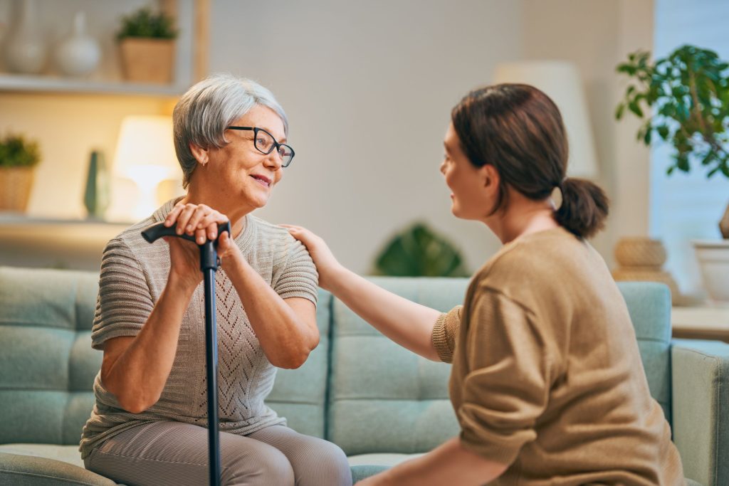 קשישה יושבת על ספה ומולה מטפלת