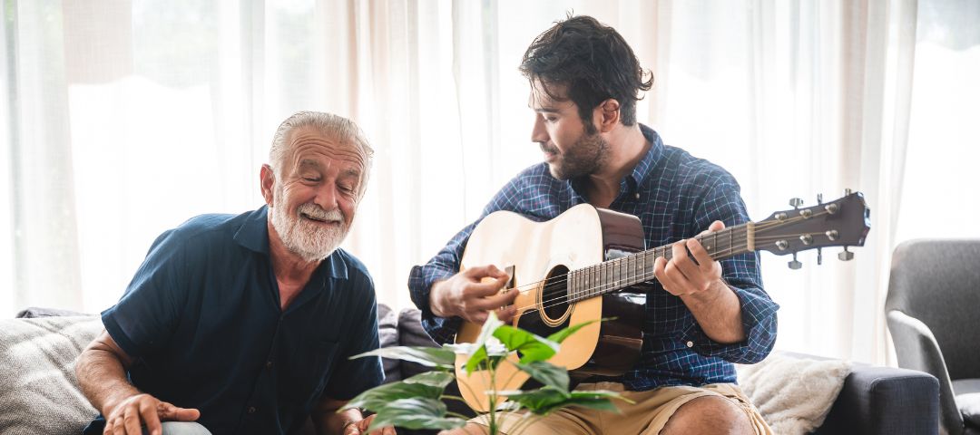בחור צעיר מנגן בגיטרה לקשיש בביתו