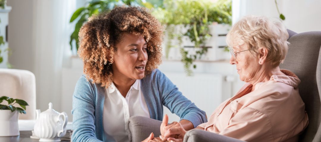 קשישה יושבת על כורסא ולידה מטפלת