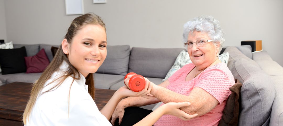 קשישה בתרגיל משקולות בישיבה ולידה מטפלת