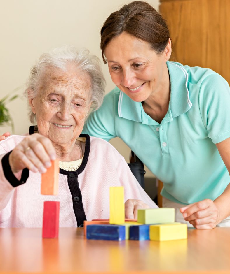 קשישה בונה מגדל מקוביות עם המטפלת שלה