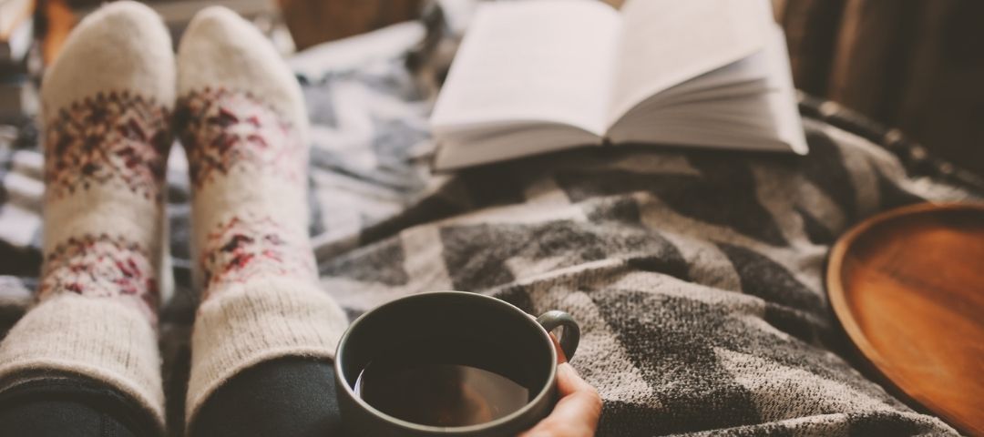זוג כפות רגליים עם גרביים חמים וכוס קפה ביד