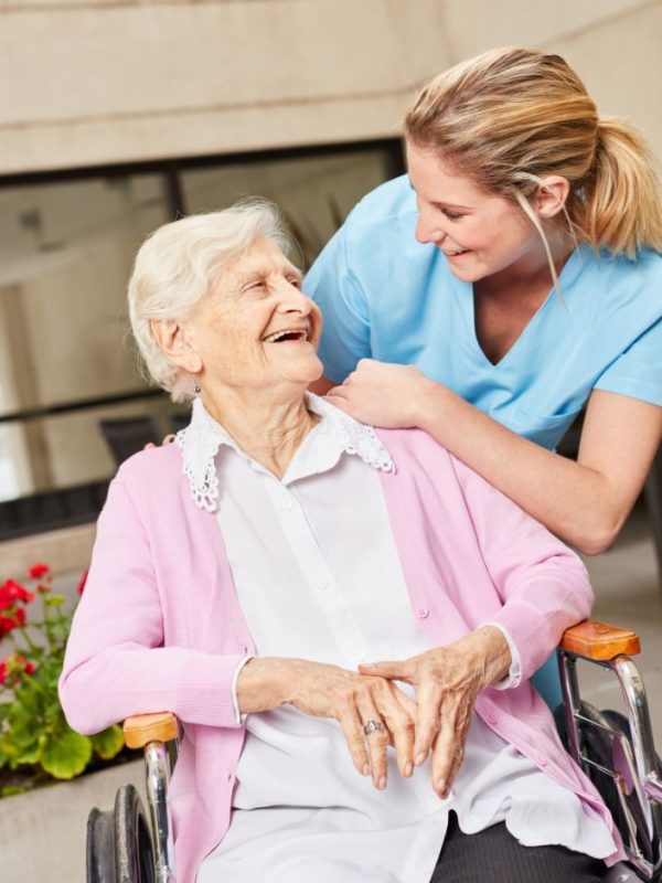 קשישה בכיסא גלגלים ומאחוריה מטפלת