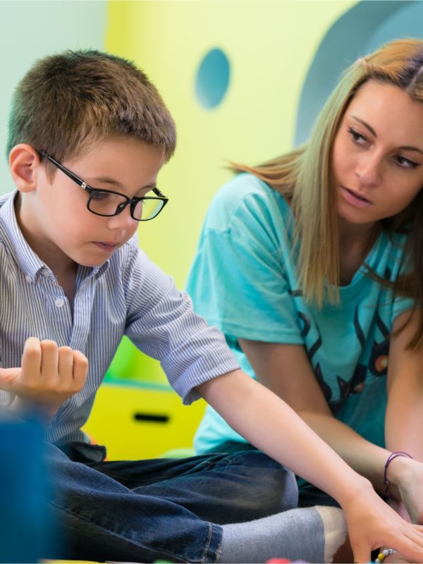 ילד בגן וסייעת או גננת יושבת לידו