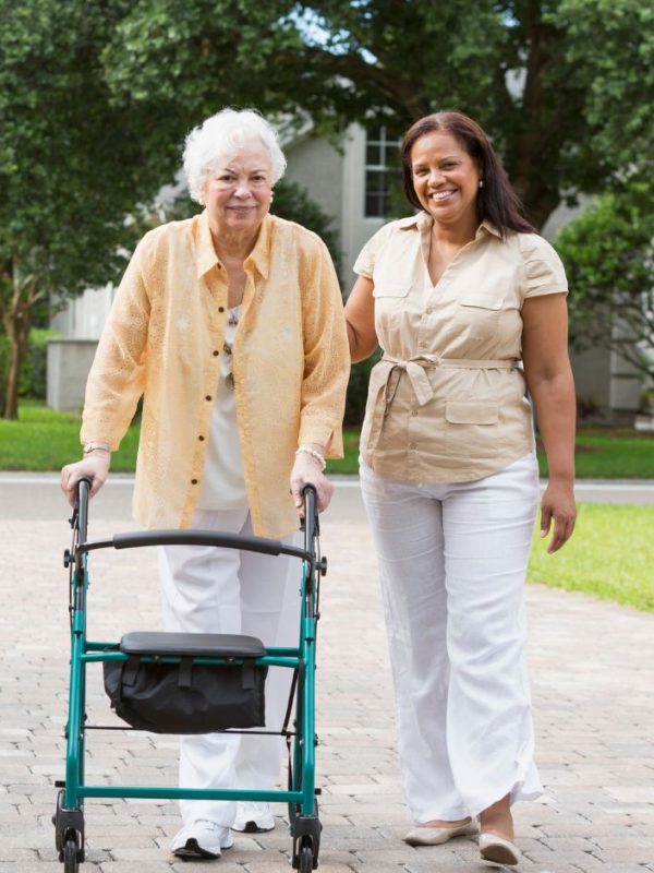 קשישה עם הליכון הולכת ולצידה מטפלת