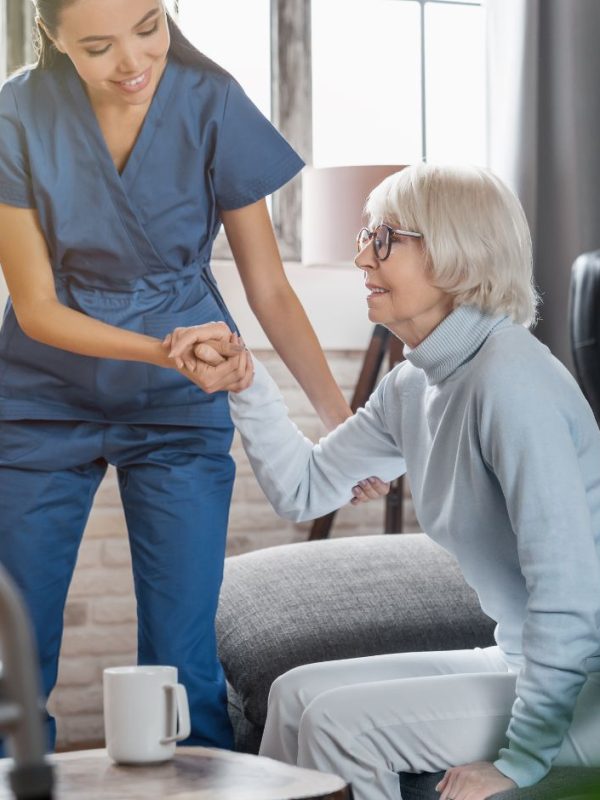 מטפלת עוזרת לקשישה לקום מהספה