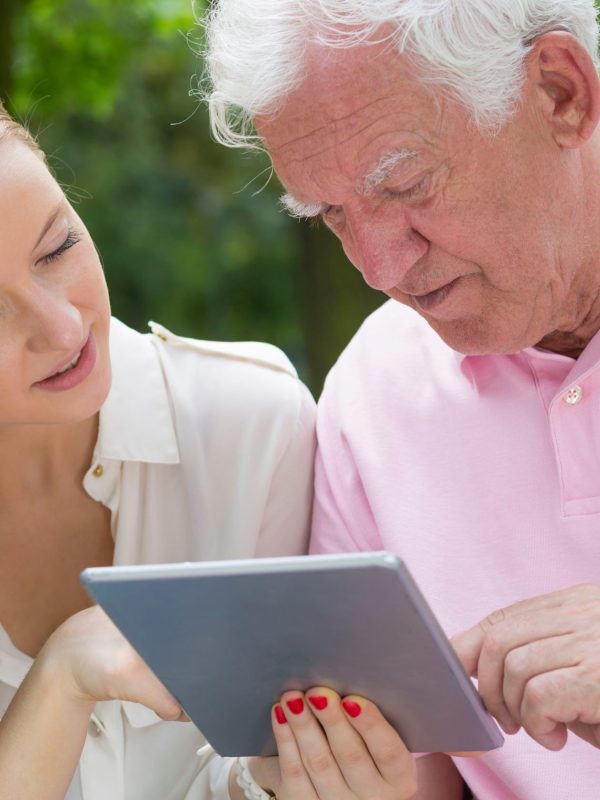 קשיש מסתכל בטאבלט ולידו מטפלת